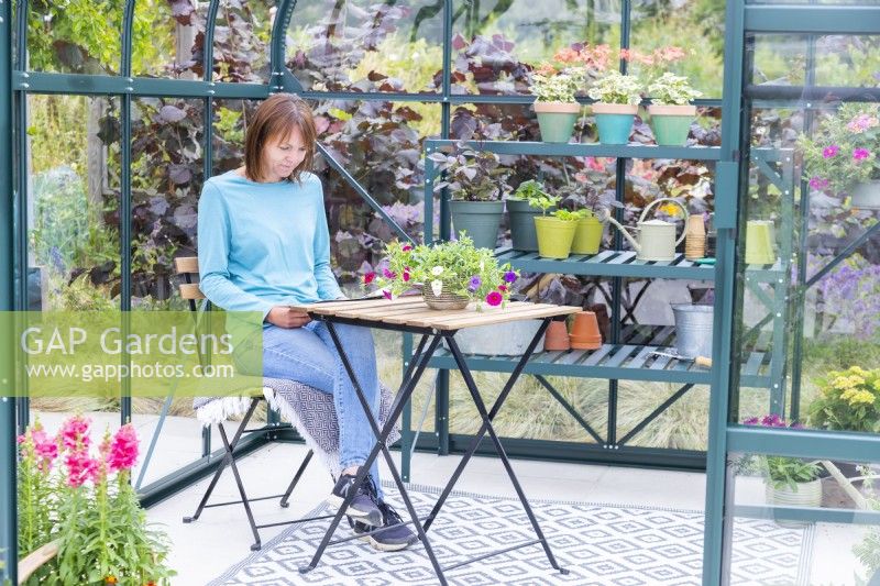 Woman sitting in greenhouse reading magazine