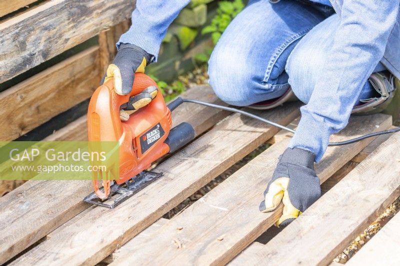 Woman sawing one plank off the back of a pallet