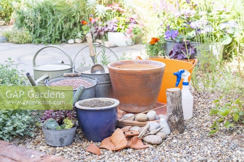 Terracotta pot and dish, cobbles, succulents, compost, gravel, sand, crocks, log, spray bottle, watering can, dowel and a trug laid out on the ground