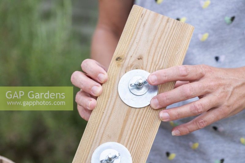 Woman fixing the pots to the wooden plank using washers, wingnuts and bolts