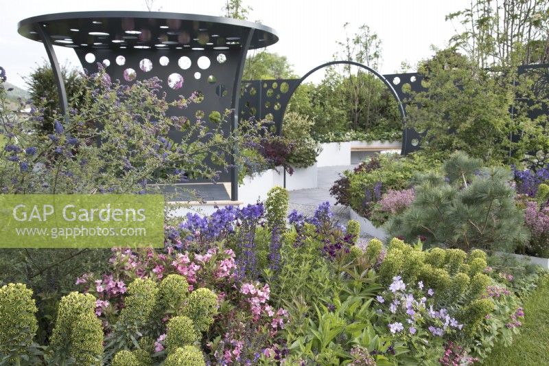 Metal pergola and moongate amongst colourful planting in the CRUK Legacy Garden at RHS Malvern Spring Festival 2022