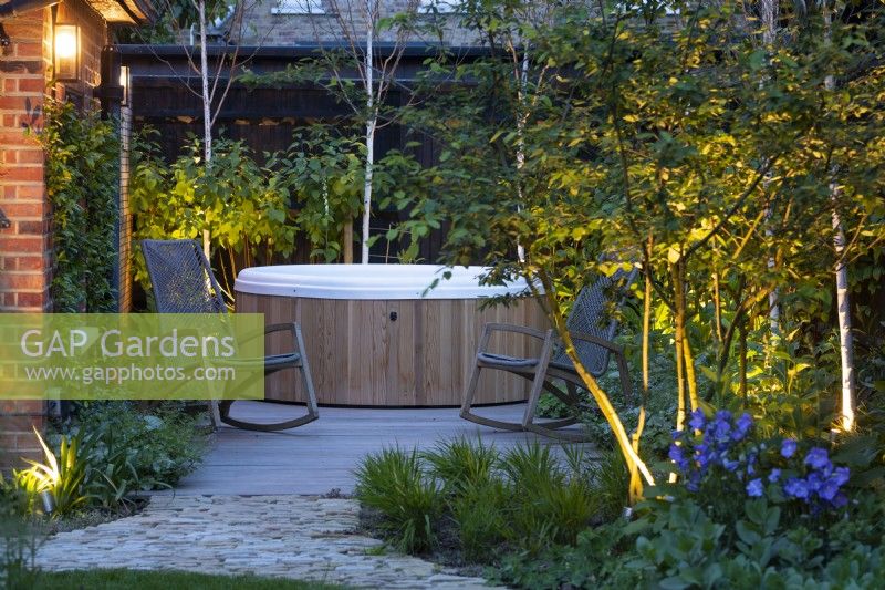 Illuminated hidden garden with jacuzzi and rocking chairs in the evening.