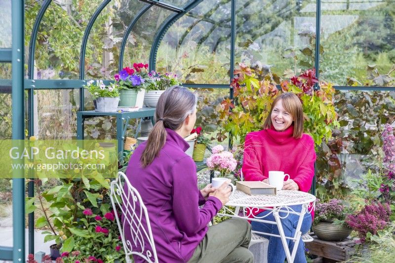 Women sitting at a table and chatting in a greenhouse filled with various plants and containers