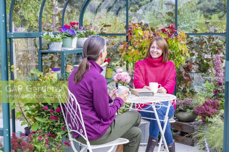Women sitting at a table and chatting in a greenhouse filled with various plants and containers