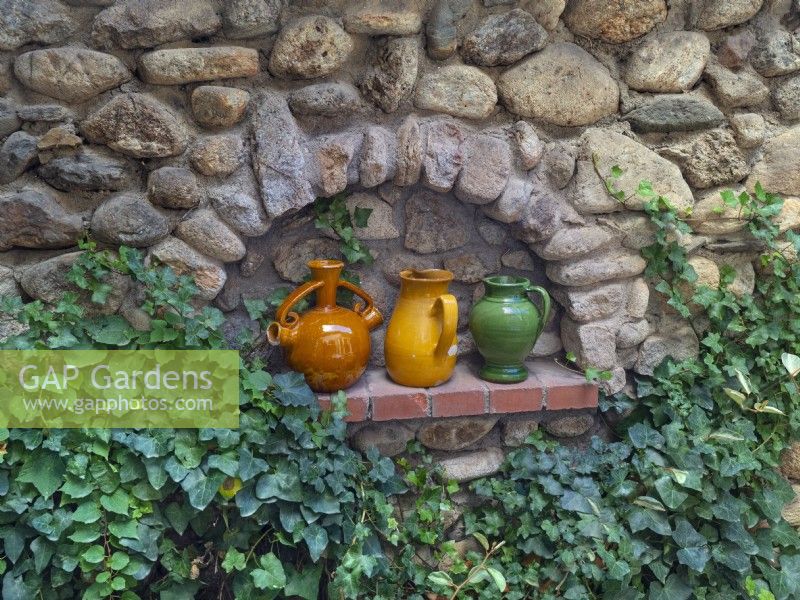 Pottery wine jugs decorate alcove in stone garden wall