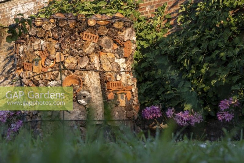 The bug hotel, created out of logs, terra cotta bricks and pots, fir cones, hay, bamboo canes and stones, is against the wall in the orchard at West Dean Gardens.
