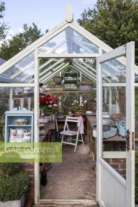 Open door in to a busy greenhouse with a wooden chair.