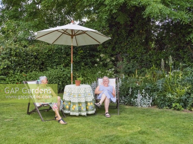 Two women sitting on deckchairs chatting in garden