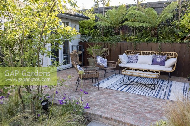 Patio with furniture in suburban garden with garden office in background
