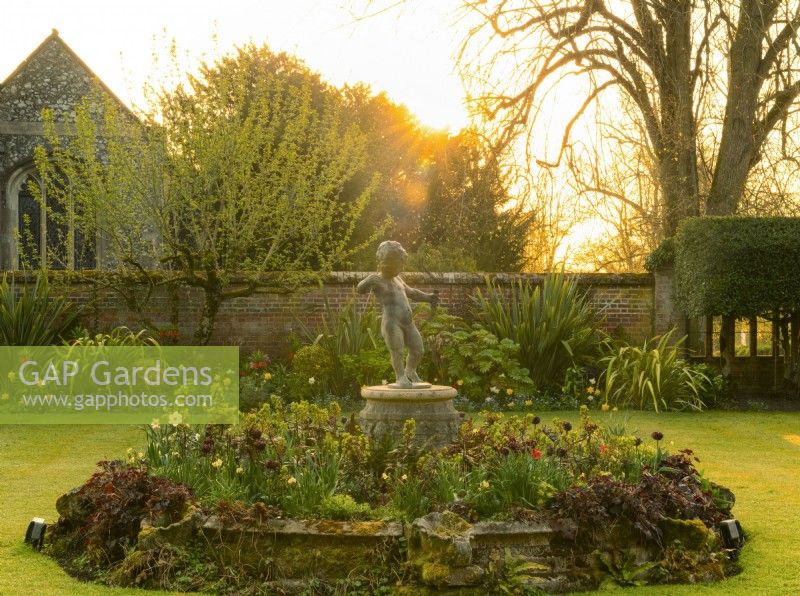 A cupid statue surrounded by Tulipa and Naricissus at sunrise in the inner court at Chenies Manor.