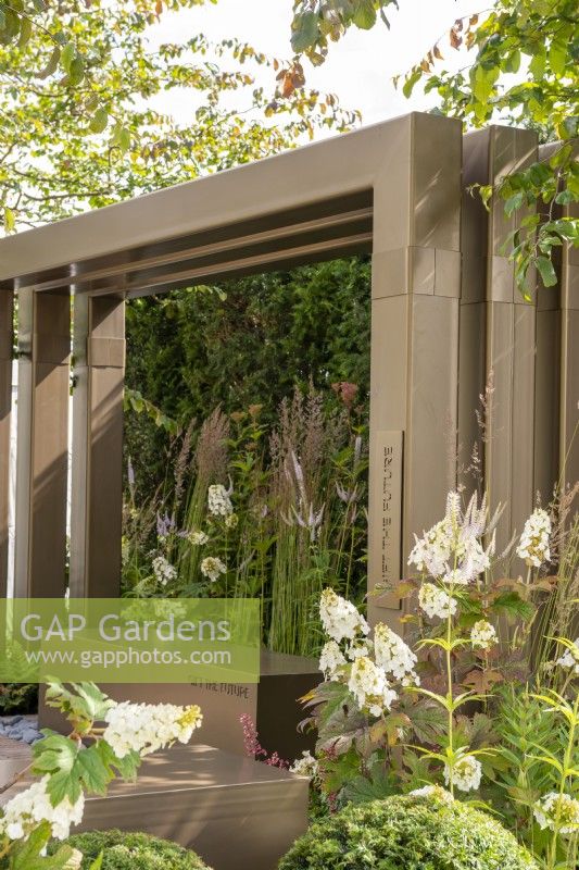 Metal pergola with box seating surroundedby grasses and Hydrangea quercifolia - Macmillan Legacy Garden: Gift the Future, RHS Hampton Court Palace Garden Festival 2022