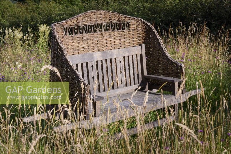 Wooden bench with a woven willow cover in the wild flower meadow at Cow Close Cottage, North Yorkshire in July full of knapweed and meadowsweet
