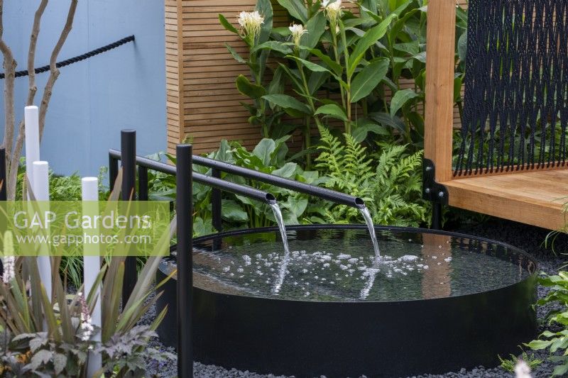 Water flowing through black spouts into a circular raised pond - The Calm of Bangkok, RHS Chelsea Flower Show 2021