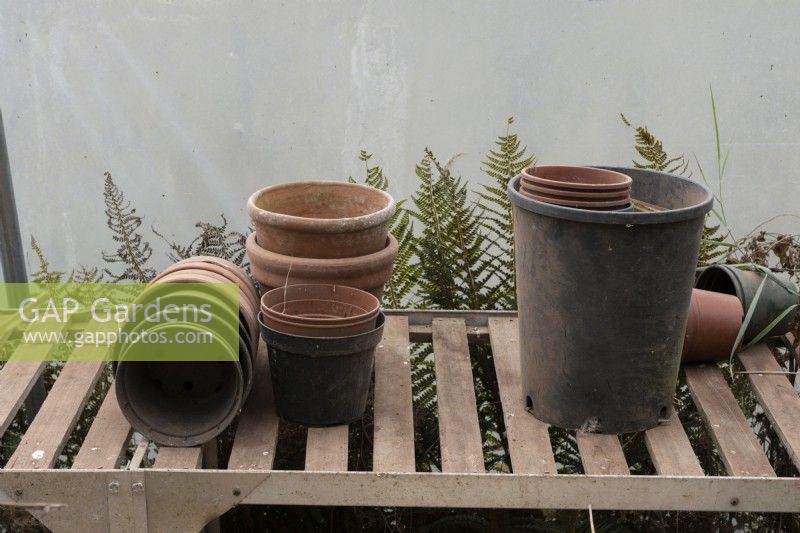 A variety of different empty pots on a wooden slatted becnh in a polytunnel. September