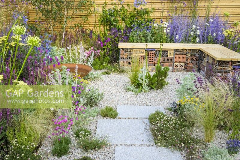 Low maintenance gravel garden with gabion bench, Corten steel water bowl and drought tolerant plants to attract pollinators, such as Salvia, Achillea, Echinops, Perovskia and Gaura surrounded by contemporary fencing - Turfed Out Garden, RHS Hampton Court Palace Garden Festival 2022