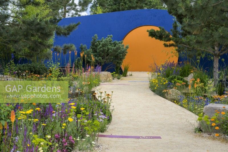 Colourful planting along curved path leading to a raising sun structure  - Over The Wall Garden supported by Takeda. RHS Hampton Court Palace Garden Festival 2022. 