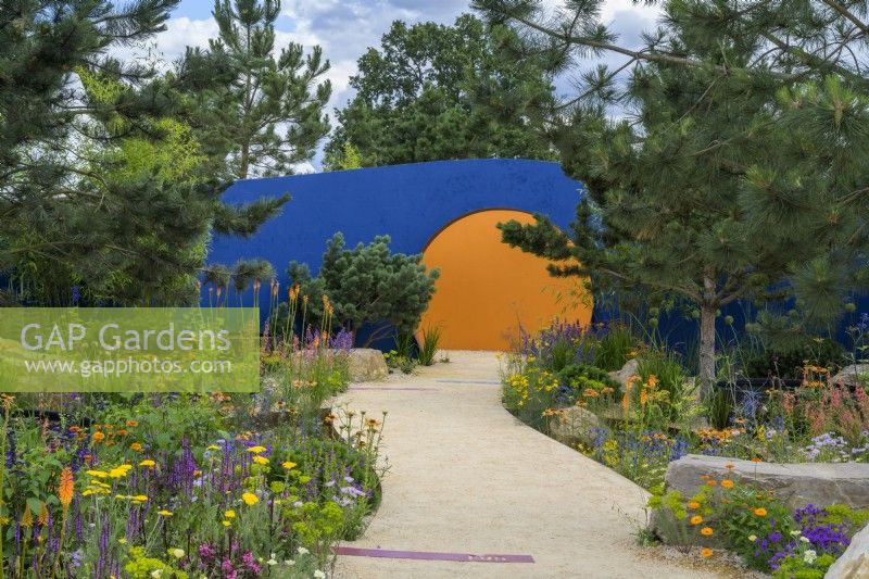 Colourful planting along curved path lading to circular opening - Over The Wall Garden, supported by Takeda. RHS Hampton Court Palace Garden Festival 2022. Designer: Matthew Childs