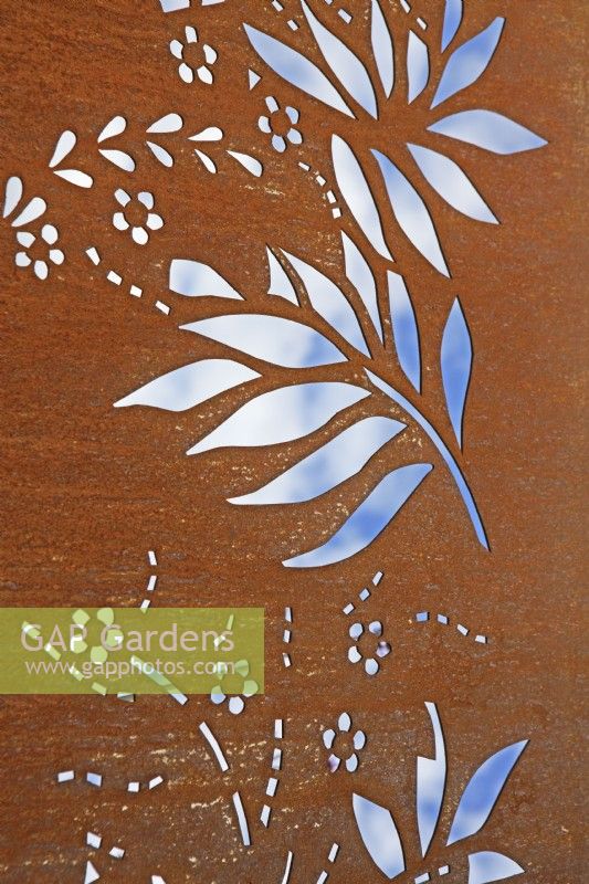 Detail of rusty Corten steel garden feature with cut-out foliage and flower patterns. July. Summer. 