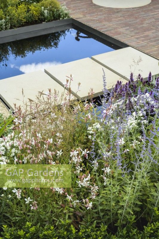 Stepping-stone bridge over rill water feature with delicate cloud planting of  Perovskia and Gaura  in The Joy Club Garden at RHS Hampton Court Palace Garden Festival 2022
