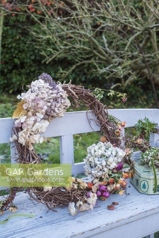 Rustic willow wreath decorated with dried hydrangeas and roses on wooden garden bench
