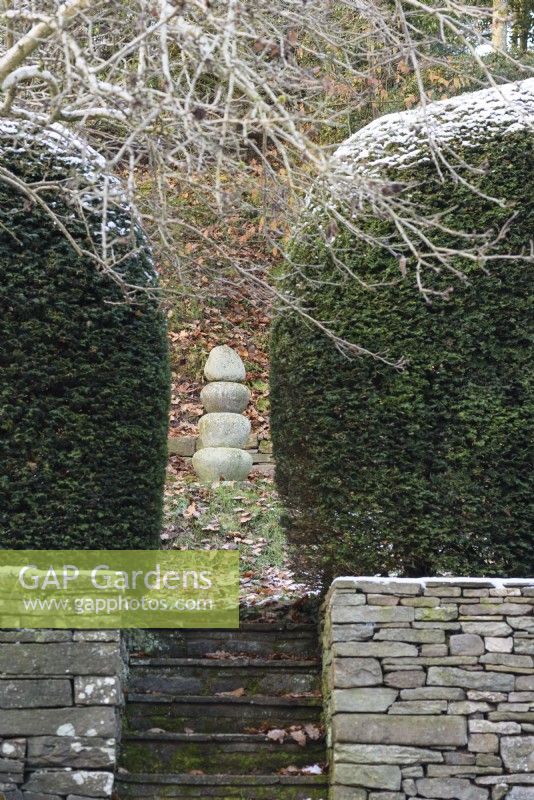Focal point of stacked stones framed by yew hedges in a garden in December.