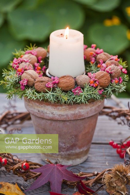 Terracotta pot with candle decorated with wreath made from walnuts, common juniper and spindle berries.