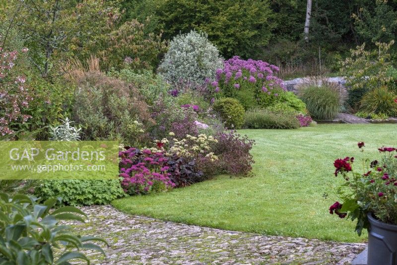The stream garden with a meandering herbaceous border planted with miscanthus, pittosporum, and perennials such as sedums, hardy geraniums, heucheras, oregano and scabious.