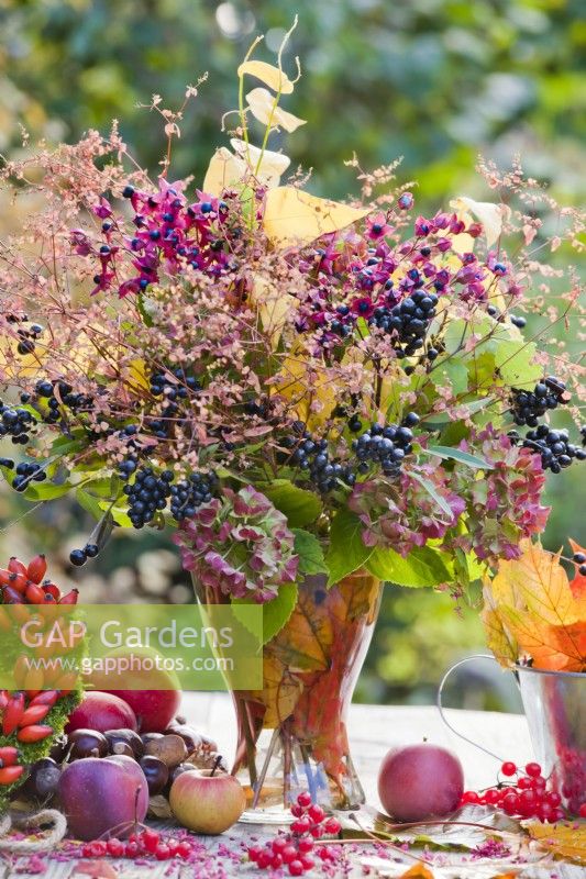 Bouquet containing hydrangea flowers, privet twigs with berries and glory tree in glass vase.