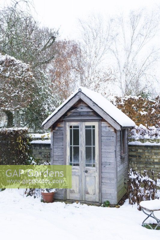 View of small summerhouse made from a restyled garden shed and salvaged doors and windows. December.