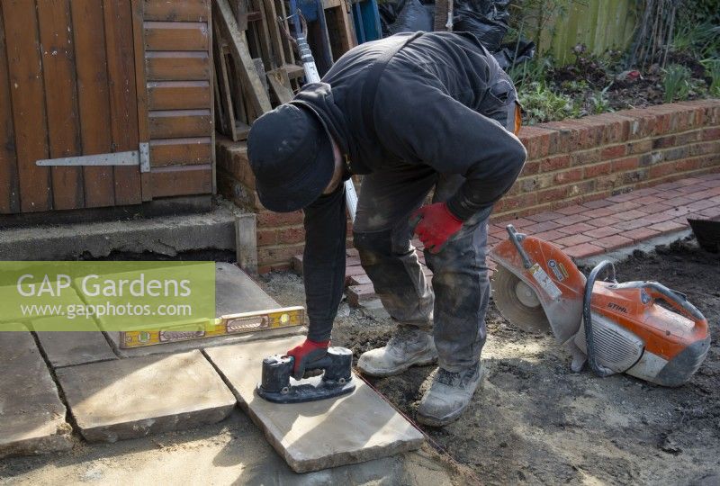 A worker using a vacuum lifter to raise a slab of York Stone for a stone terrace during the makeover of a small London garden.