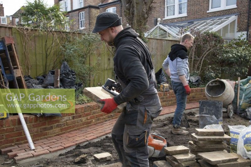 A worker carrying a slab of York Stone being used to construct a terrace during the makeover of a London garden.