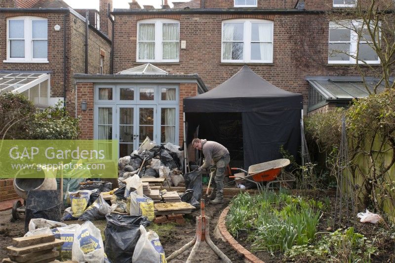 Construction materials and a worker at the start of the makeover of a small London garden.