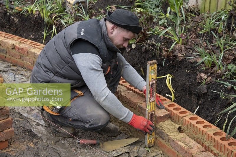 A worker building a low brick wall around a raised bed during the makeover of a small London garden.