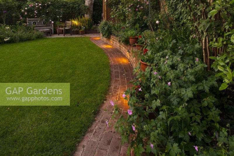 A London garden in June after a makeover in February with a new brick path and low wall creating a new space for containers
next to the raised bed.
