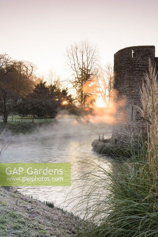 Morning sun illuminates mist rising from the moat at The Bishop's Palace in Wells in January.
