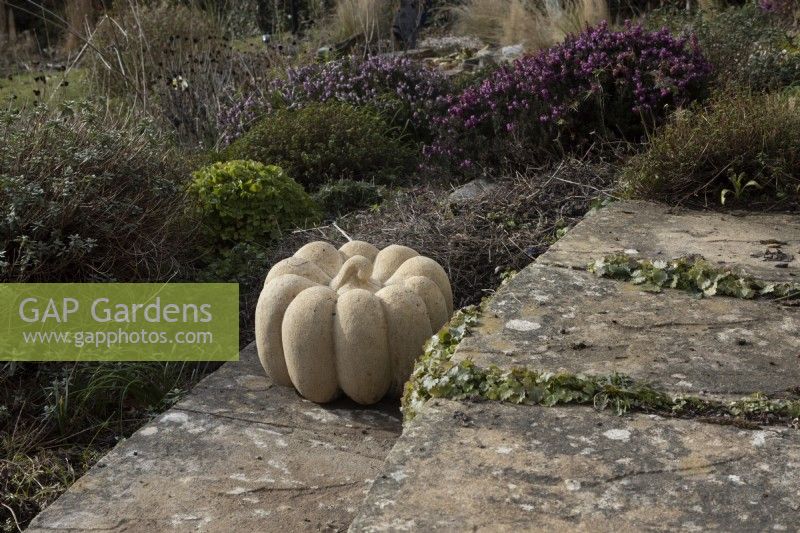Pumpkin, a Bath stone scultpure, made by Zoe Singleton, set on the edge of a paved step with heather sin the background. 