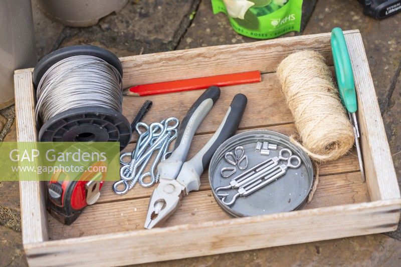 Wire, tape measure, pencil, string, scossors, pliers, eyelets screws, tensioners, ferrules and thimbles laid out in a wooden tray