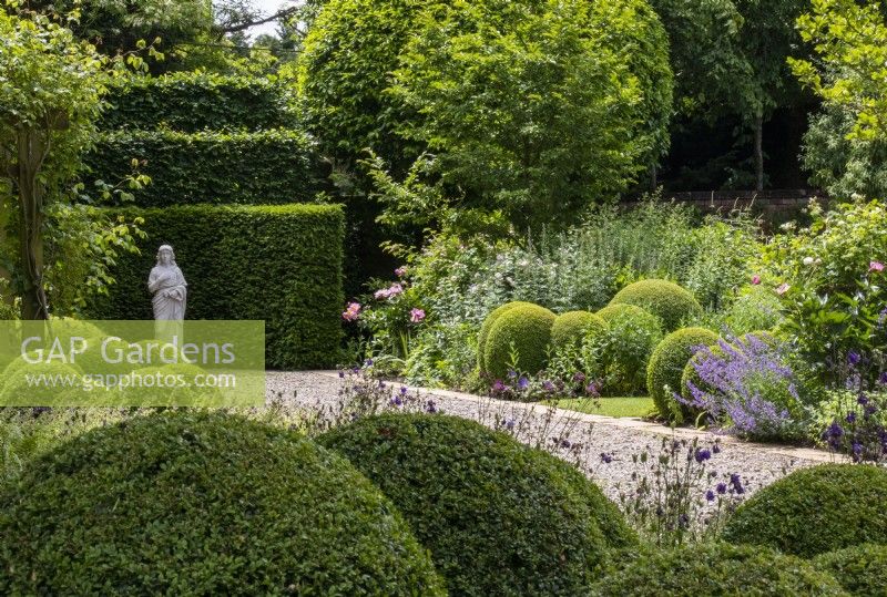 Clipped buxus balls and mixed borders in The South Garden at Morton Hall with a classical statue in the background.