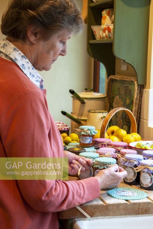Woman applying gingham tops to jars of preserves and tying with rafia