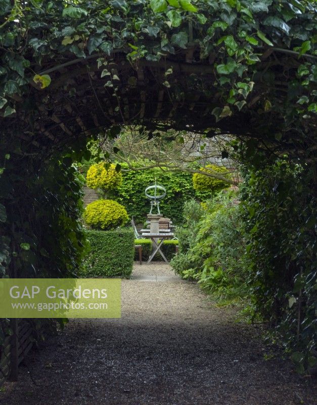 View down an Ivy tunnel to the Armillary Sun Dial with Clipped Buxus - Box - hedging and topiary in the tea garden at - East Ruston Old Vicarage, Norfolk May Spring