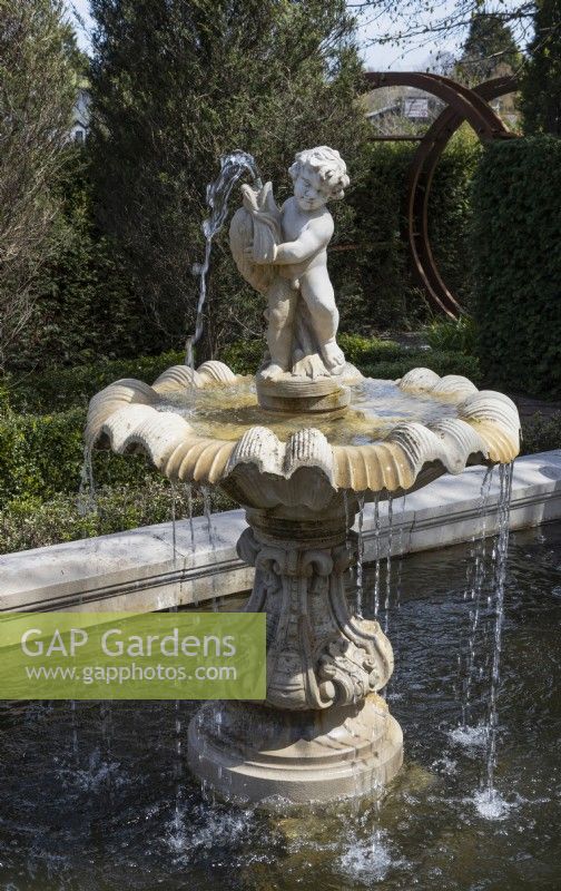 The Italian White Garden's classical fountain and formal pool. A Moorgate is in the background. Trago Mills show gardens, Devon, UK. May. Spring