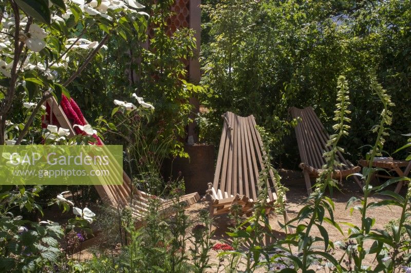 Group of wooden slatted chairs in clearing with trees and shrubs around - The Beauty in Small Spaces - BBC Gardeners' World Live 2023 - Designers TJ Kennedy and Kerianne Fitzpatrick