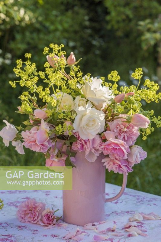 Pink and white roses with Alchemilla mollis displayed in a pink china jug on printed tablecloth