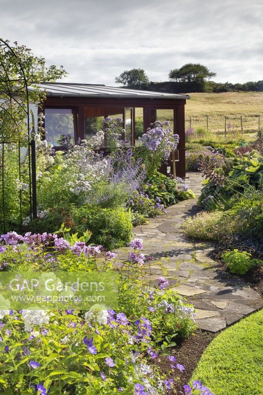 White and purple themed perennial border, featuring phlox and campanula, by crazy paving path to conservatory