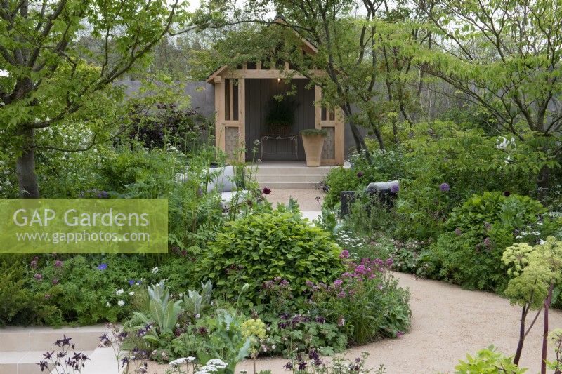 A winding path leads between borders planted with a range of trees, shrubs and perennials to foster biodiversity, passing a seating area before arriving at a timber summerhouse.