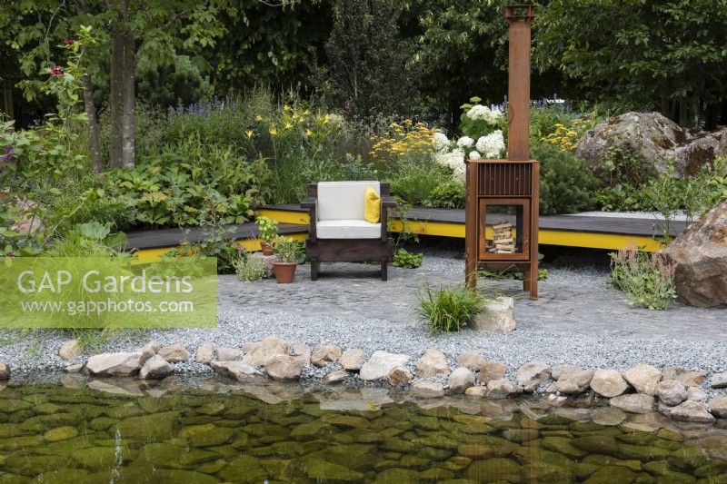 A waterside terrace is built in reclaimed granite setts, and edged in a reclaimed timber boardwalk edged in a border of leafy shrubs and perennials.