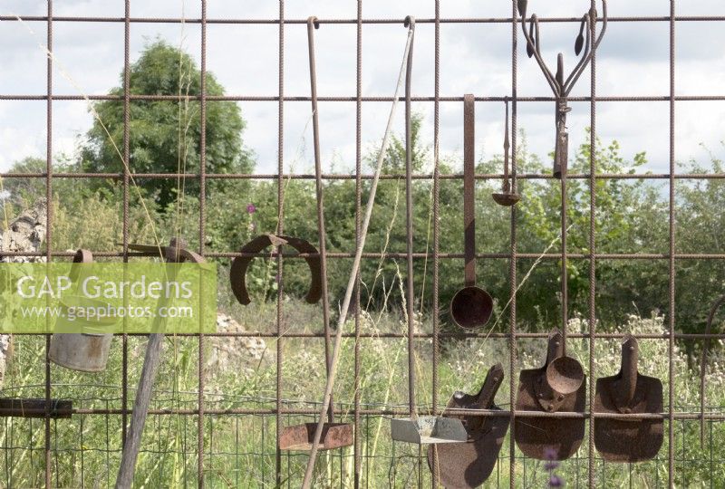 Old rusted garden tools hanged on concrete mesh.