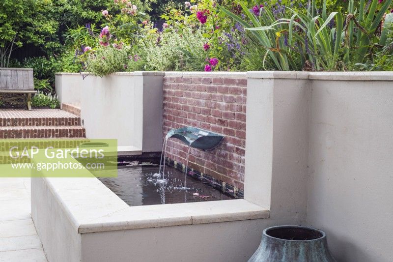 White rendered and brick raised pool with verdigris basin fountain with borders above 