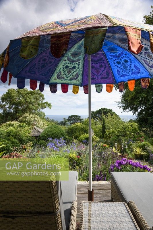 Loungers below a colourful umbrella in a coastal garden in July