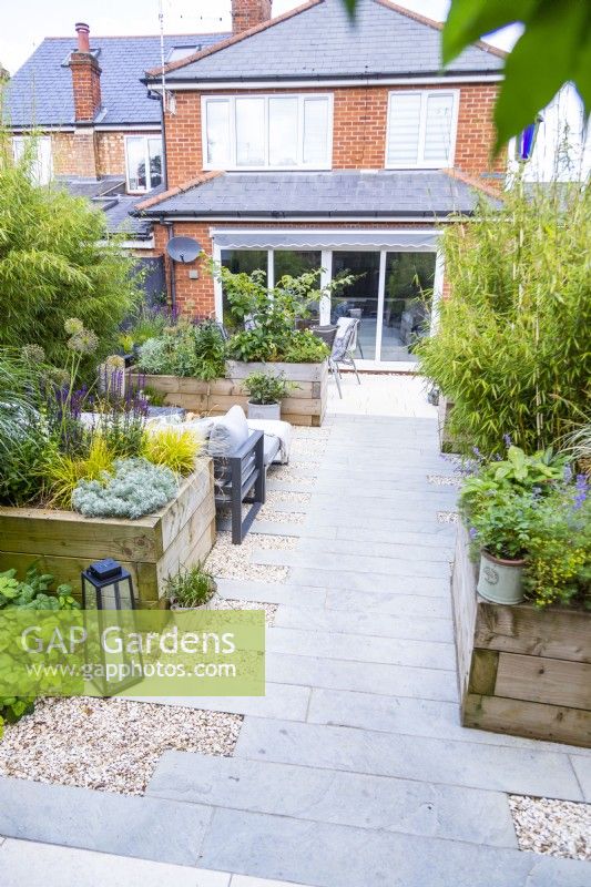 Staggered stone tile path leading from end of garden towards the house past multiple raised beds and a seating area